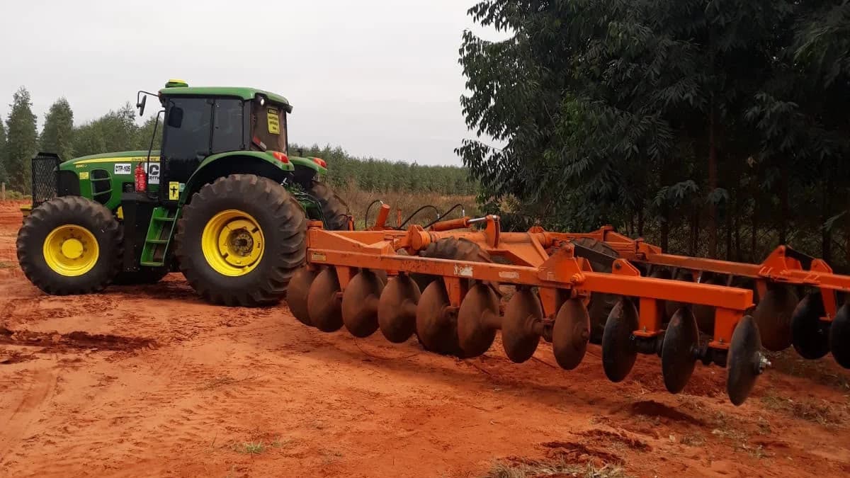 Trator da Cerne Florestal acoplado a uma grade aradora, parado em estrada de terra ao lado do plantio