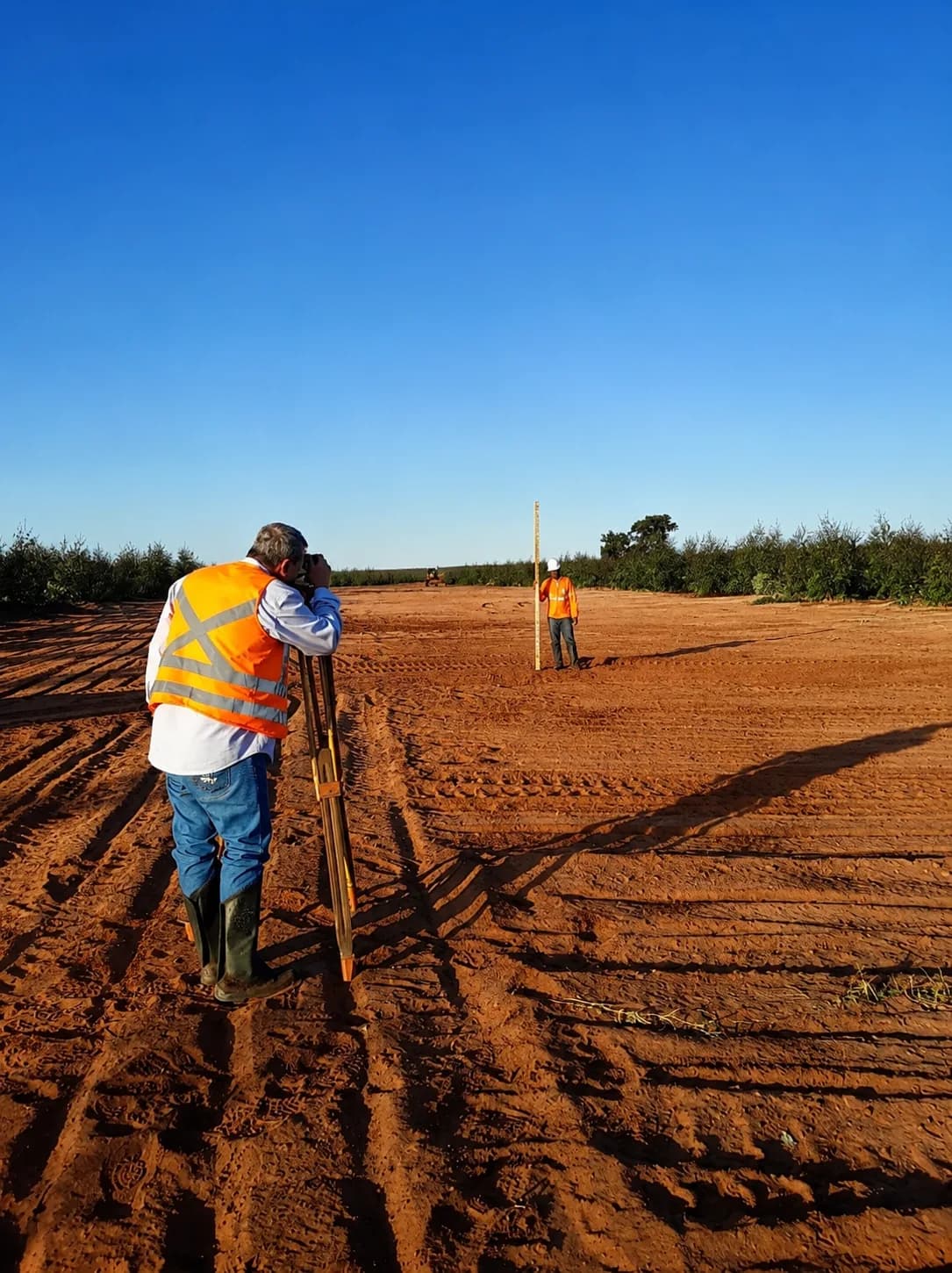 Equipe e equipamento de topografia em atividade de campo, em área de solo exposto